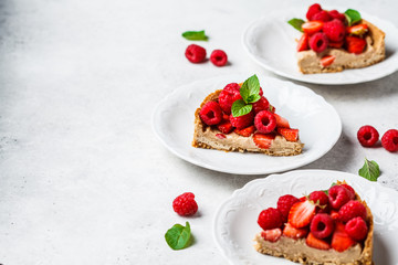 Pieces of berry tart with raspberries, strawberries and cream on white plates.