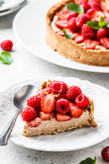 Piece of berry tart with raspberries, strawberries and cream on white plate.