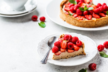 Piece of berry tart with raspberries, strawberries and cream on white plate.