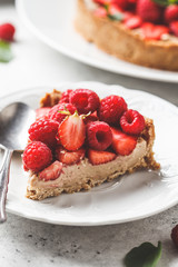 Piece of berry tart with raspberries, strawberries and cream on white plate.