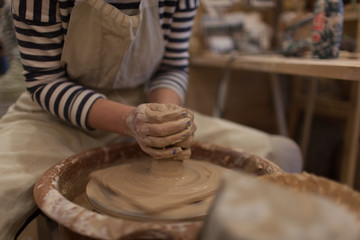 Potter working on potters wheel making ceramic pot from clay in pottery workshop