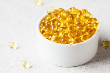 Fish oil capsules (omega 3) in white bowl on gray background.