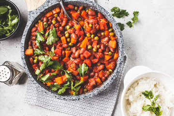 Vegan bean stew with tomatoes in a pan over white background.