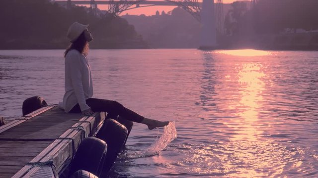 Woman on river bank enjoying a warm evening, swinging bare feet, Summer beach