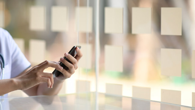Cropped image of doctor using mobile phone in hands in office