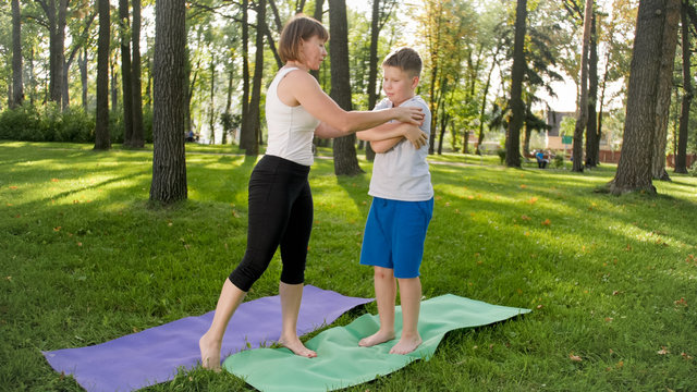Image of middle aged woman teaching teenage boy doing yoga and fitness on grass at park. Family taking care of their health