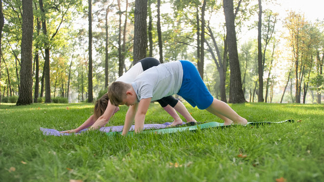 Portrait Of 12 Years Old Boy Doing Yoga Exercise With His Mother At Park. Family Meditating And Stretching At Forest