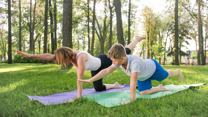 Portrait of 12 years old boy doing yoga exercise with his mother at park. Family meditating and stretching at forest