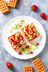 Belgian waffles with fruits strawberries and kiwi on white plate closeup. Tasty breakfast