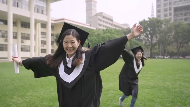 slow motion Group japanese girl friends having fun running on green meadow summer graduation day. young asian women college students wear gown and cap. female mortarboard fall down on grass campus