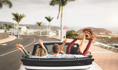 Happy friends having fun in convertible car on vacation - Young millennial people driving on cabriolet in summer holidays - Transport and youth lifestyle concept - obrazy, fototapety, plakaty