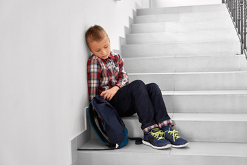 Depressed boy sitting on staircase of primary school. 