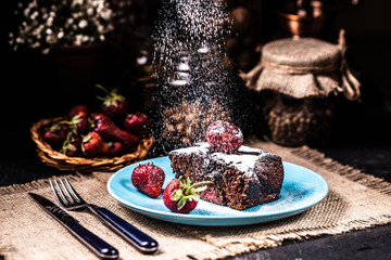 A slice of brownie with strawberries on a blue plate. Sugar snow.