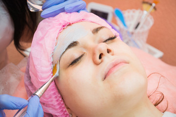 The procedure of applying cleansing mask on the face of a young girl