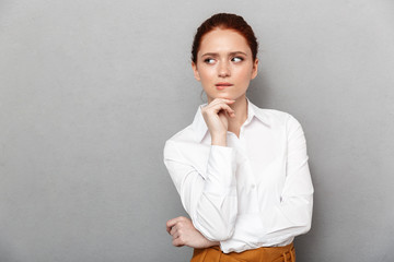 Portrait of professional redhead businesswoman 20s in formal wear touching her chin and posing in office