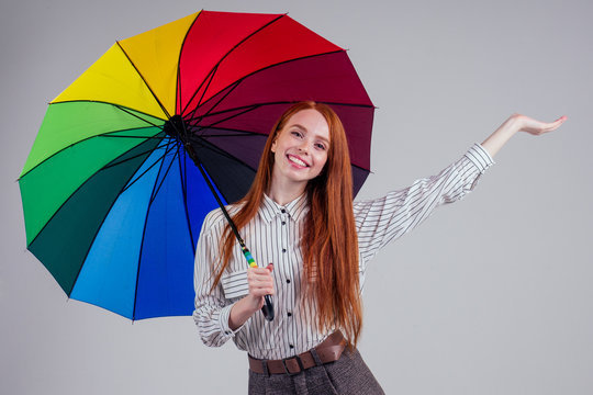 beautiful redhead girl on a white background in the style striped shirt with rainbow an umbrella. autumn fashion look seasonal spring sale