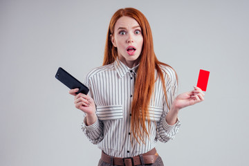 Naklejka premium red-haired businesswoman in a striped shirt happy using mobil phone and holding a red plastic card (cardboard) on white background studio black friday sale