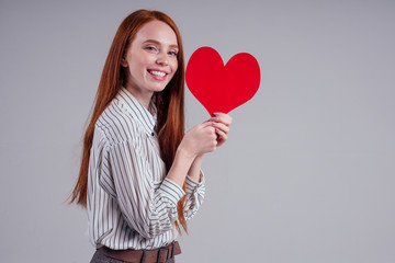 Happy redhead girl businesswoman in a striped shirt model sending air kiss with decorative hearts Valentines Day gift on white background studio