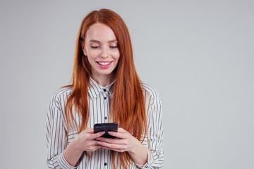 Fototapeta premium Cheerful redheared woman businesswomen in a striped shirt showing blank smartphone screen white background studio