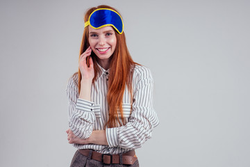 Good Morning. Smiling redhead young business woman in a striped shirt and blue yellow sleep mask white background studio
