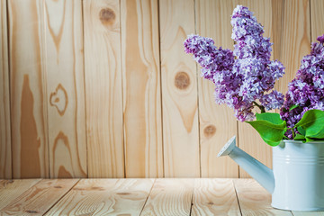 flowers of lilac in white watering can on wood