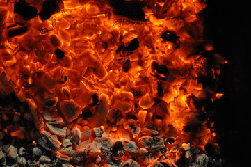 Vibrant red orange color flaming texture with smoldering pieces of firewood and blazing flames. Bonfire closeup in darkness. Coal fireplace abstract background.