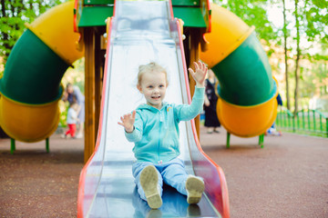 Fototapeta na wymiar Adorable little girl 4 years old having fun on a slide in a playground in the summer day.