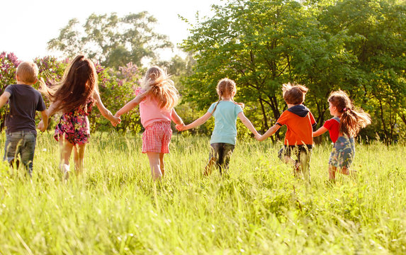a group of children playing and running in the park on a green gozon.