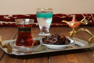 Traditional oriental cousine. Ramadan food. Dates, tea in glass on platter, taboulah salad, flat bread (aish) water and carpet roll background.