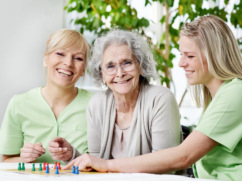 Seniorin spielt mit Pflegepersonal ein Brettspiel