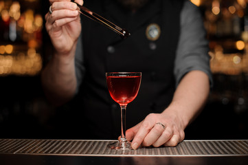 Male bartender adding a one red berry with tweezers to the cocktail
