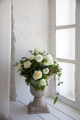 bouquet of white artificial roses, eucalyptus and ivy in a stone vase on the windowsill near the window