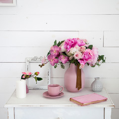 bouquet of orchids, peonies, roses in a ceramic vase on the bedside table and a stack of books
