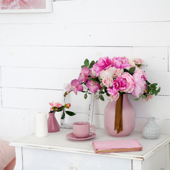 bouquet of orchids, peonies, roses in a ceramic vase on the bedside table and a stack of books