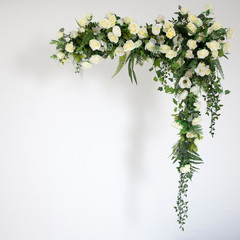 White framing frame of artificial flowers, anemones, roses, eucalyptus and ivy for a wedding ceremony hanging on wall