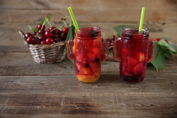 Berries and citrus infused water cocktail, compote, lemonade or tea. Summer iced cold drink with berries, cherry, lemon on a wooden rustic background with branch of cherry. With copy space for text.