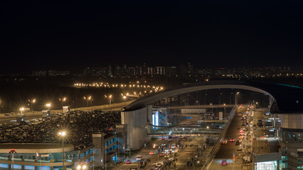Fototapeta na wymiar Night shot of intense car traffic on the road with overpass and full multilevel parking lot