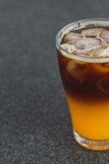 cold brew coffee with orange juice. Glass with cold coffee and ice on the background of a bag  and chaotically scattered coffee beans and orange. Selective focus