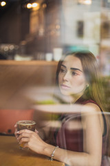 beautiful girl holds a glass of cold coffee mixed with ice and orange juice on cafe background. Selective focus