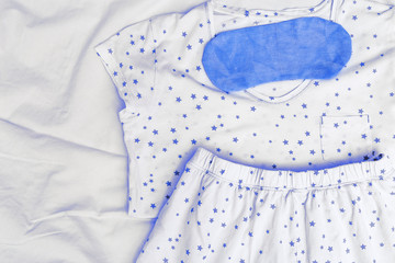 Light pajamas on bed and blue sleep masks. Nightwear on white sheet. Top view. Flat lay.