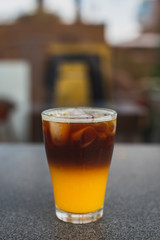 cold brew coffee with orange juice. Glass with cold coffee and ice on the background of a bag  and chaotically scattered coffee beans and orange. Selective focus