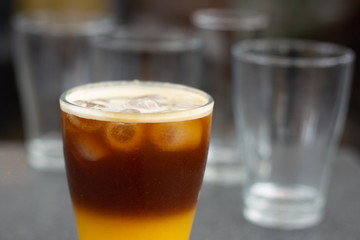 cold brew coffee with orange juice. Glass with cold coffee and ice on the background of a bag  and chaotically scattered coffee beans and orange. Selective focus