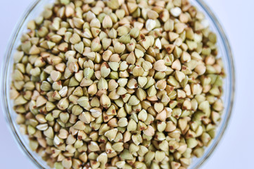Green buckwheat untreated in a glass bowl for a healthy lifestyle on a white background.