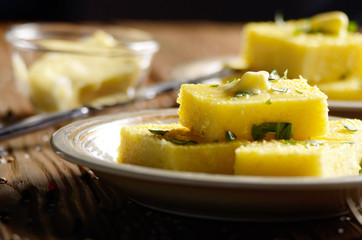 Polenta with butter and greens on clay dish on wooden rustic table