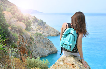 Tourist girl with backpack sitting on a stone and looking on a seascape horizon.