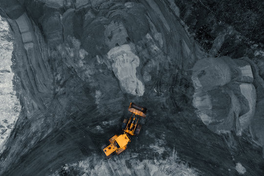 Yellow excavator or bulldozer in coal open cast mining quarry, industrial extraction of minerals, aerial top view