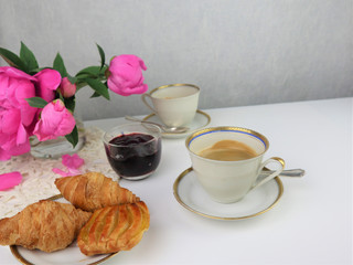 breakfast with two cups of coffee and croissants, bouquet of pink flowers