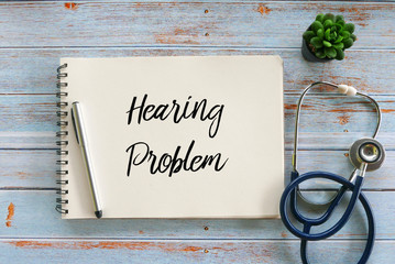 Top view of stethoscope,plant,pen and notebook written with Hearing Problem on wooden background.