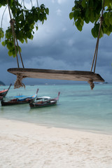 Swing hang from tree over beautiful tropical island view with boats on the sea and sky background. Exotic vacation on Amazing Koh Lipe in Thailand