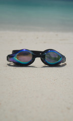 Fototapeta na wymiar Swim goggles on sandy beach over lagoon sea background. Travel, holiday, tropical vacation concept